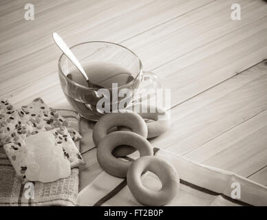 La composizione della bevanda di tè in una grande ciotola e alcuni dolci sul tavolo. I cookie di grano, bagel. Foto in bianco e nero. Foto Stock