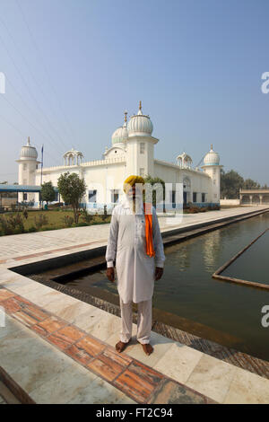 Un anziano Sikh indossando un turbante giallo e bianco salwar kameez dal santo piscina al Gurdwara Lakhi giungla nel Punjab (India). Foto Stock