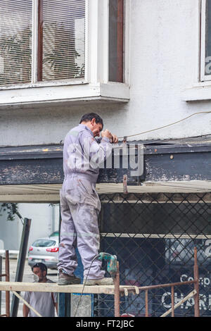 Uomo che ripara un tetto, PUERTO MONTT, Cile - circa nel novembre 2015. Un operaio, in piedi su un ponteggio, è riparare un overhangi Foto Stock