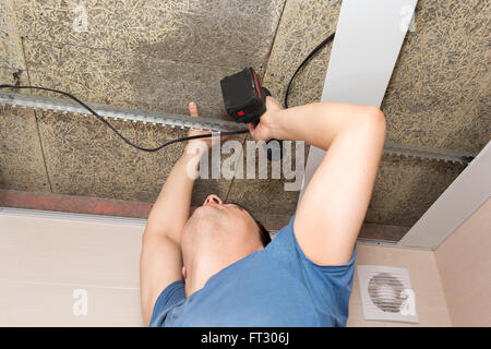 L'uomo aziona le viti nel soffitto della fibra di legno con un cacciavite Foto Stock