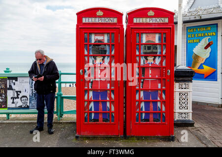 Un uomo testi con uno smartphone accanto a due tradizionali cabine telefoniche rosse, Brighton East Sussex, Regno Unito Foto Stock