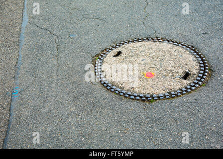 Tombino coperchio di scarico su terreni accidentati oldasphalt street a Foto Stock