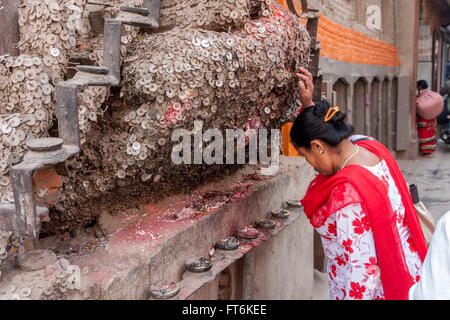 Il Nepal, Kathmandu. Donna che prega per nessun mal di denti al santuario per il mal di denti Dio, Bangemudha Square. I chicchi di riso e red ku Foto Stock