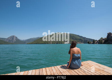 Giovane donna seduta sul molo e godere la vista del lago Foto Stock