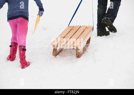 Un padre tira una slitta di legno su una ripida collina dopo runnign in discesa con i suoi figli Foto Stock