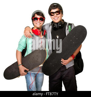 Due skateboarders felici ascoltando la musica nelle cuffie alla moda indossando vestiti urbani e occhiali da sole isolato su sfondo bianco Foto Stock