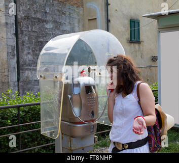 Donna che parla in una cabina telefonica, gesticulating all'aperto Foto Stock