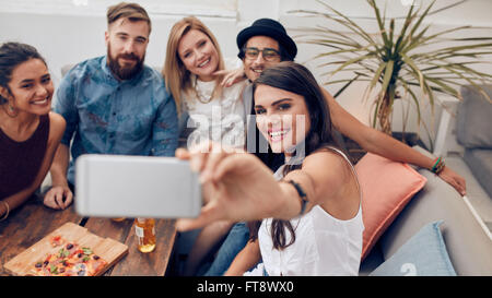 Multirazziale persone di godere in parte prendendo un autoritratto con il telefono cellulare. Un gruppo di giovani amici seduti sul divano tenendo se Foto Stock