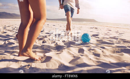 Sezione bassa ritratto di giovani che giocano a calcio sulla spiaggia. Gli amici che giocano a calcio sulla spiaggia sabbiosa, concentrarsi sulla palla e gamba Foto Stock