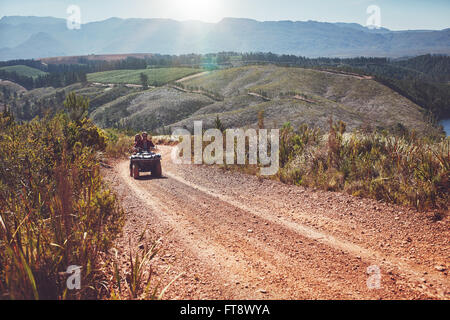 Vista di un giovane alla guida di un ATV su strada sterrata in campagna. Giovane uomo e donna in sella a una moto quad sulla strada di campagna. Foto Stock