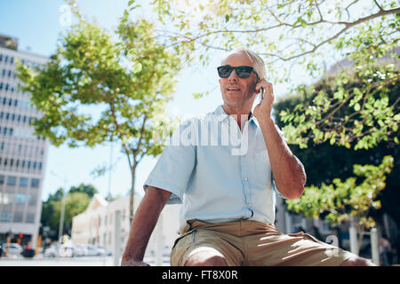 Coppia uomo caucasico seduta oudoors nella città di effettuare una telefonata. Tourist al di fuori della città utilizzando il telefono cellulare. Foto Stock