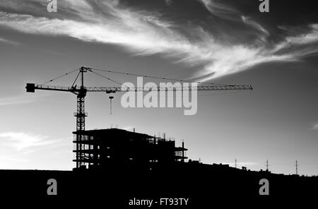 Una foto in bianco e nero di gru da cantiere sotto il cielo con le nuvole. Foto Stock