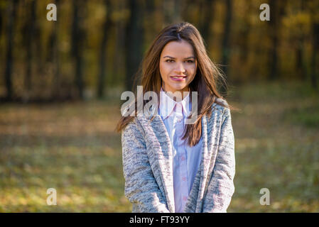 Sorridente ragazza è in posa di una foresta di autunno in un caldo camicetta a maglia. Azione si svolge in un pomeriggio d'autunno. Foto Stock