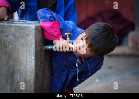 Una giovane ragazza bhutanesi acqua potabile direttamente da un rubinetto a Gangte nella valle di Phobjikha, Bhutan Foto Stock