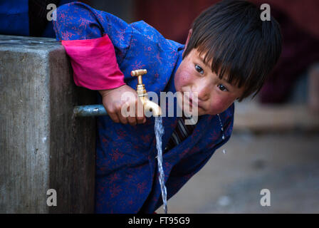 Una giovane ragazza bhutanesi acqua potabile direttamente da un rubinetto a Gangte nella valle di Phobjikha, Bhutan Foto Stock