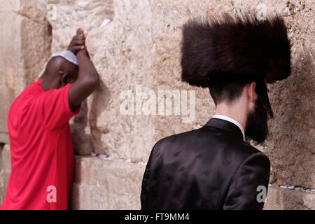 Ebreo Hasidic indossando una pelliccia shtreimel cappello indossato da molti sposato Haredi uomini ebraica, su Sabato e festività ebraiche e un ebreo etiope pregando nel muro occidentale o Kotel nella città vecchia di Gerusalemme Est Israele Foto Stock