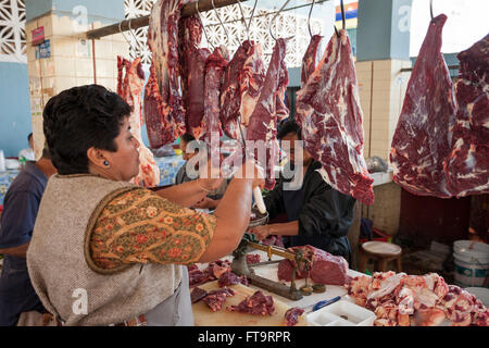 Rendendo cottura carni bovine sul mercato. Una donna del macellaio fette una striscia di carni bovine provenienti da un grande appeso pezzo di carne di manzo. Foto Stock