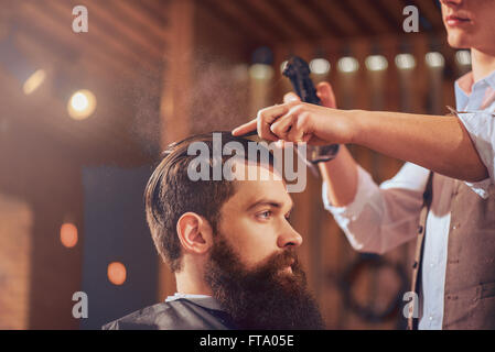 Professional barbiere per lo styling dei capelli del suo cliente Foto Stock