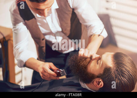 Professional barbiere il taglio di barba di piacevole uomo Foto Stock