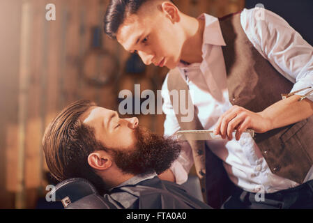 Professional barbiere per lo styling dei capelli del suo cliente Foto Stock