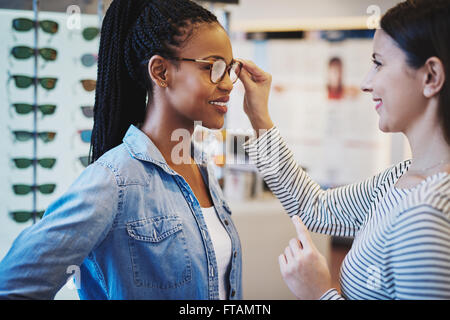 All'ottico optometrista aiutando un grazioso client africana di provare e acquistare telai per un paio di occhiali Foto Stock