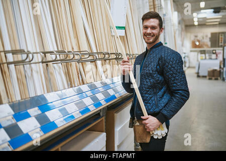 Felice fiducioso giovane falegname tuttofare o in piedi in un negozio di ferramenta acquisto di lunghezze di tagliare il legname dalle cremagliere Foto Stock