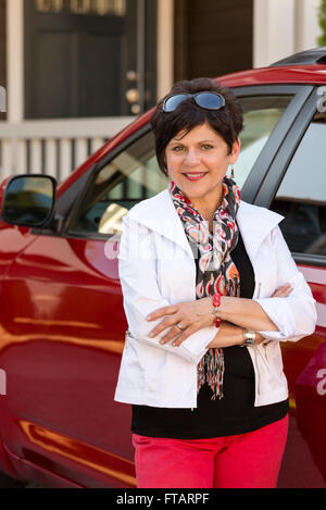 Ritratto di un felice, fiducioso, maturo, di mezza età professional donna in piedi accanto a auto nei pressi di una casa o di home Foto Stock
