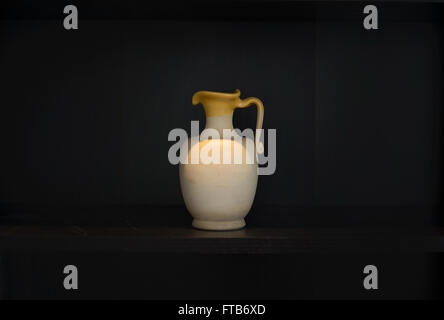 Caraffe di terracotta terracotta oggetto domestico con impugnatura a mano al buio su un ripiano isolato sul nero, chiaroscuro. Foto Stock