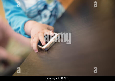 Piccolo bambino giocoso canto di raggiungere per telefono cellulare sul tavolo. Foto Stock