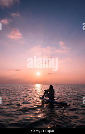 L'uomo a guardare il tramonto su un paddleboard, Meeru, Maldive Foto Stock