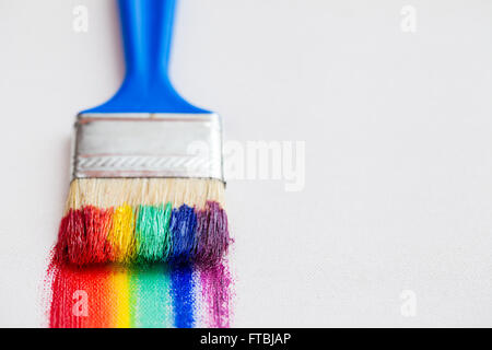 Primo piano del pennello e pennellate multicolore dell'arcobaleno su tela bianca Foto Stock