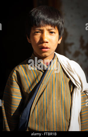 Ritratto di un giovane ragazzo bhutanesi indossando un tradizionale striped gho (accappatoio) nel villaggio Nimshong, southern Bhutan Foto Stock