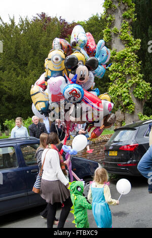 Donna che mantiene un grande grappolo di fantasia elio palloncini pieni di passeggiate lungo la strada con alcuni bambini piccoli Foto Stock