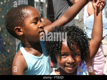 South African bambini danza alla musica dalla radio auto su una strada comunale al di fuori della loro scuola. Foto Stock