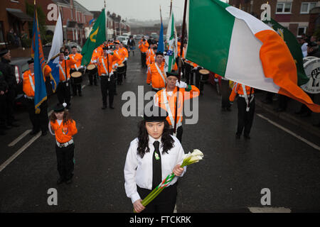 Falls Road, Belfast, Regno Unito 27 marzo 2016 una ragazza con un tradizionale Pasqua Lilly con l'Eire Nua (Nuova Irlanda) banda di flauto dietro. la band ha preso parte in salita di Pasqua centenario commemorazione Parade Credito: Bonzo Alamy/Live News Foto Stock