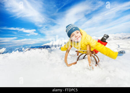 Little Boy giaceva sul sorriso della slitta e far scorrere verso il basso Foto Stock