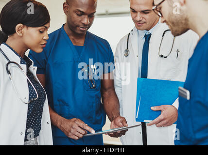 Il gruppo di medici e multirazziale consulenza permanente i record paziente su un computer tablet, vista ravvicinata Foto Stock