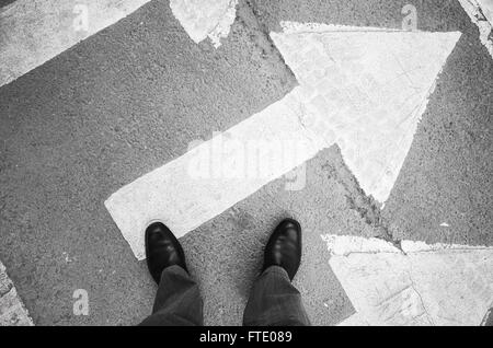 Urbanite man in black nuovi fulgidi scarpe di cuoio in piedi sul passaggio pedonale la segnaletica stradale con frecce bianche Foto Stock