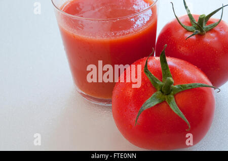 Bicchiere di succo di pomodoro con due pomodori. Chiudere la vista. Foto Stock