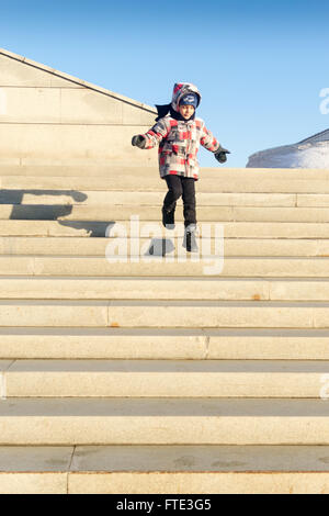 UFA - RUSSIA 20Febbraio 2016 - un giovane bambino in un caldo abbigliamento invernale salta con gioia verso il basso una linea di fasi come i suoi genitori frequentare un Foto Stock