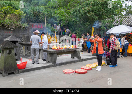 Giovane donna cinese pregando con la masterizzazione di bastoncini di incenso nella sua mano nella parte anteriore di un santuario. Haikou, Hainan in Cina. Foto Stock