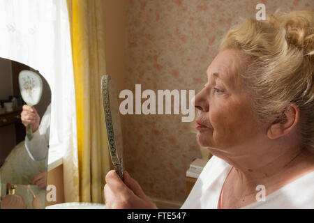 Signora anziana guardando il suo riflesso in uno specchio. Foto Stock