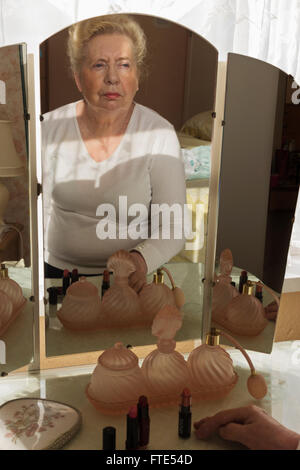 Signora anziana guardando la sua riflessione in un vecchio tavolo specchio. Foto Stock