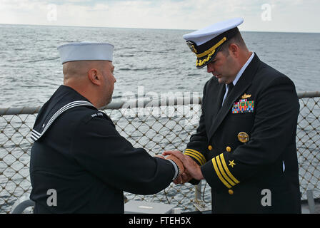 Mar Nero (ott. 11, 2014) - Fire Controlman 1a classe David Santino mani della Cmdr. Dennis Farrell, comandante, il proiettile involucri dal 21-gun salute sparato durante una cerimonia commemorativa per onorare le vittime dell'Ottobre 12, 2000 attentato terroristico a bordo del Arleigh Burke-class guidato-missile destroyer USS Cole (DDG 67) stand presso l'attenzione. Cole, homeported a Norfolk, Virginia, sta conducendo operazioni navali negli Stati Uniti Sesta flotta area di operazioni a sostegno degli Stati Uniti per gli interessi di sicurezza nazionali in Europa. Foto Stock