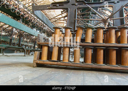 Bobine in legno accanto alle antiche attrezzature in giro del secolo la seta gettando fabbrica. Foto Stock