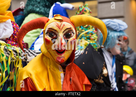 Un partecipante del Carnevale di Basilea 2016 dissimulata come un arlecchino clown in rosso e giallo costume guarda direttamente la fotocamera Foto Stock