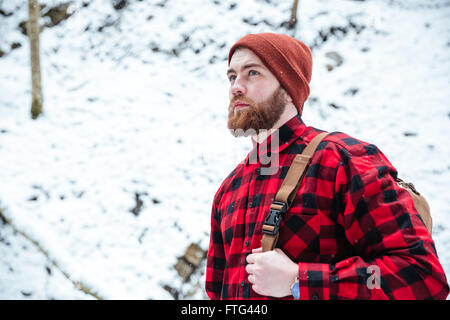 Riflessivo barbuto giovane con zaino in montagna in inverno forest Foto Stock