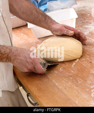 Baker preparare una pagnotta di pane con un raschietto e la sua mano per forma e formare la pasta su un contatore di legno Foto Stock