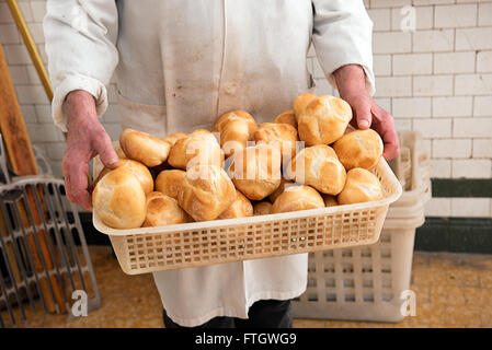 Baker tenendo un cesto pieno di pane appena sfornato crostini di pane bianco rotoli nel suo mantello bianco al forno Foto Stock