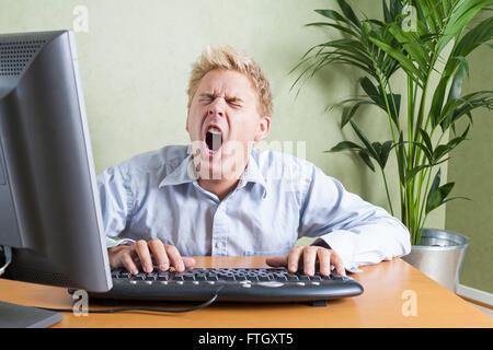Stanco uomo sbadigliare quando si lavora nella parte anteriore del computer in ufficio Modello di Rilascio: Sì. Proprietà di rilascio: No. Foto Stock